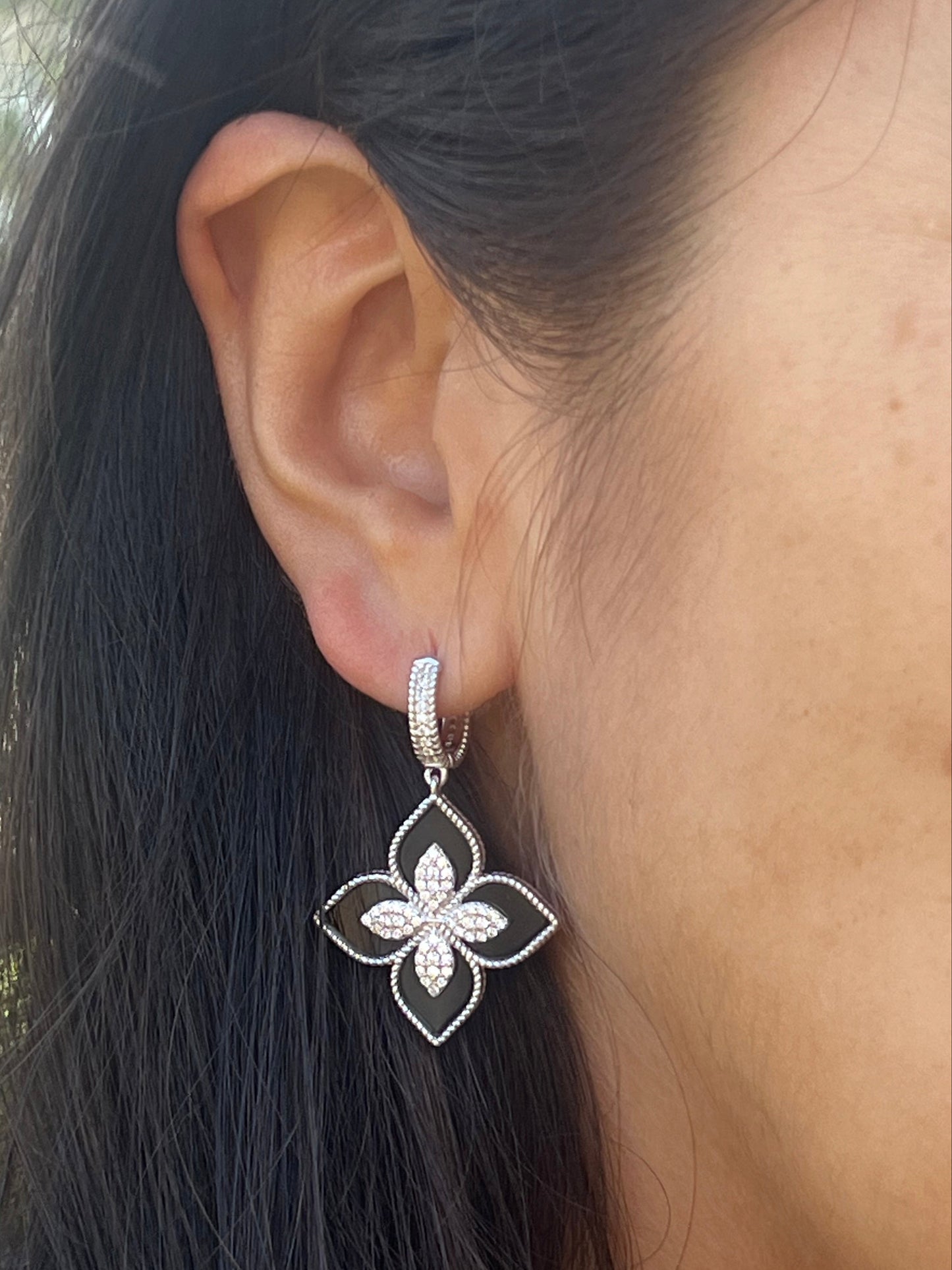 Close-up of an ear wearing a silver earring with a floral design.
