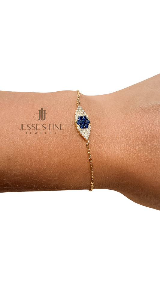 A gold chain bracelet with a central blue flower-shaped gemstone surrounded by small clear stones, shown worn on a person's wrist against a white background. The brand name 'Jesse's Fine Jewelry' is visible as a watermark on the skin.
